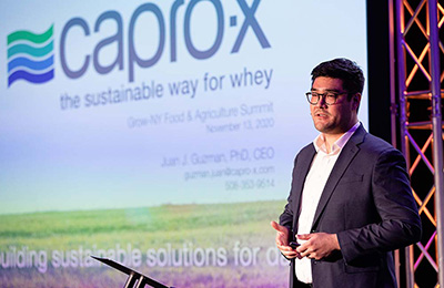 Juan Guzman, co-founder of Capro-X, presents his startup pitch at the 2019 Grow-NY competition. In the background, is a slide with his company's logo.